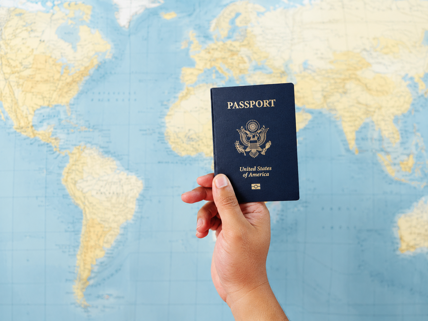 Hand holding a U.S. passport in front of a light blue world map